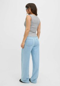 Top senza maniche grigio abbinato a jeans a gamba larga blu chiaro. I jeans presentano tasche posteriori e una vestibilità rilassata. La modella indossa occhiali da sole neri.