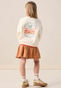 Sweatshirt crème avec un graphique de flamant rose multicolore et le texte "BEAUCOUP D'AMOUR". À associer avec une jupe orange et des baskets à accents verts.