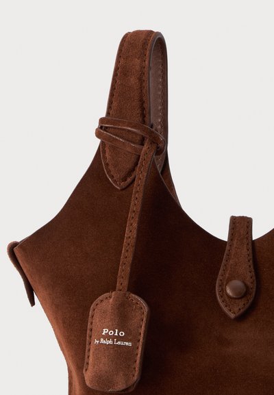 Κοντινό πλάνο καφέ σουέτ τσάντας Polo από Ralph Lauren με χειρολαβή στην κορυφή και δερμάτινη ετικέτα προσαρμοσμένη κοντά στη χειρολαβή.