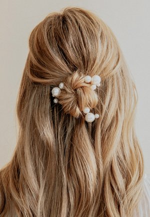 Accessorio per capelli con un bun attorcigliato, decorato con grandi pere bianche e piccoli dettagli. I capelli biondi mossi e texturizzati completano il design.