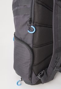 Sac à dos en nylon noir avec un motif en grille texturé, des accents en mesh, plusieurs compartiments zippés et des tirettes de fermeture éclair bleues.