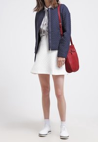 Giacca bomber trapuntata blu navy, abito A-line bianco con texture, borsa rossa, scarpe bianche e calzini bianchi. Completo casual moderno con colori a contrasto.