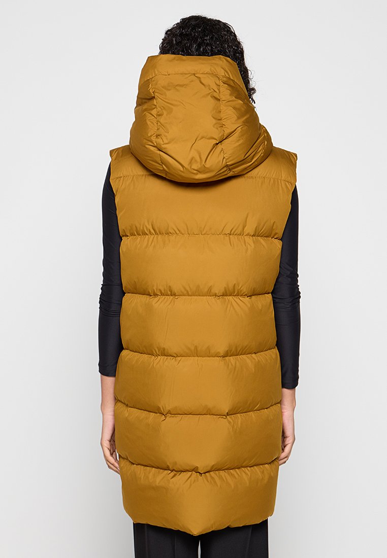 Bezrękawnik puchowy w kolorze złotym, z wysokim kapturem, pikowanym wzorem i lekko zwężającym się dolnym końcem, co nadaje nowoczesny kształt.