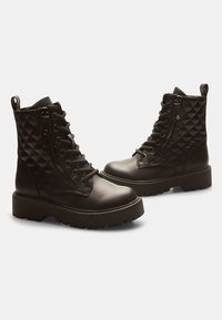 Botines negros de cuero sintético con un patrón acolchado, punta redonda, cordones en la parte frontal y cremallera lateral, con una suela gruesa.