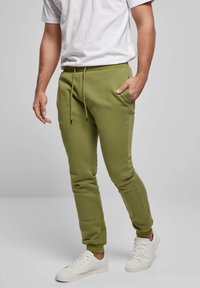 Grüne Jogginghosen aus Baumwollmischung mit elastischem Bund, Kordelzug, seitlichen Taschen und zulaufenden Beinen, kombiniert mit weißen Sneakern.