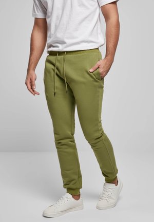 Grüne Jogginghosen aus Baumwollmischung mit elastischem Bund, Kordelzug, seitlichen Taschen und zulaufenden Beinen, kombiniert mit weißen Sneakern.