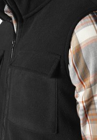 Schwarze Fleece-Weste mit Reißverschluss, ausgestattet mit zwei Fronttaschen, getragen über einem karrierten Hemd in bunten Orange- und Beige-Tönen.