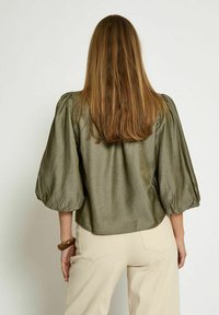 Olive green, short-sleeve blouse with puffed sleeves and a slightly cropped hem, made from a smooth, textured fabric.