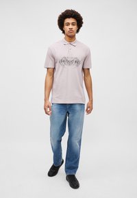 Ανοιχτό μωβ πόλο μπλούζα με γραφιστικό σχέδιο μπροστά, σε συνδυασμό με ξεθωριασμένο μπλε τζιν και μαύρα sneakers. Καθημερινό, χαλαρό στιλ.