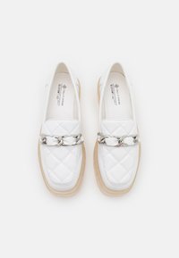 Mocassins blancs matelassés avec un accent de chaîne en argent et une semelle plateforme beige clair. Matière lisse avec un design à bout rond.