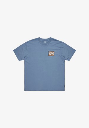 Niebieska bawełniana koszulka z krótkim rękawem, z małą kwadratową naszywką w falisty pomarańczowym, kremowym i czarnym wzorze po lewej stronie klatki piersiowej.