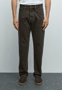 Mörkbruna denimbyxor med en avslappnad passform, femfickorsdesign och en synlig bältesöglor i midjan, ihop med bruna skor.