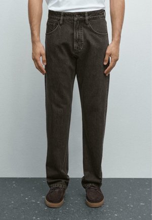 Pantaloni in denim marrone scuro con un taglio morbido, design a cinque tasche e passante per cintura visibile in vita, abbinati a scarpe marroni.