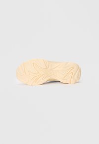 Shoe outsole featuring a wavy pattern, in light beige rubber with textured grooves. Smooth edge design enhances flexibility and grip.