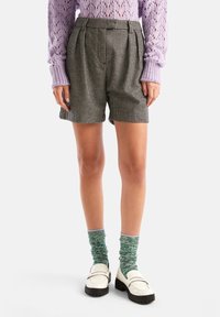 Svartspräckliga shorts med veck, kombinerat med en lavendelfärgad stickad tröja och gröna mönstrade strumpor, bärs med vita loafers.