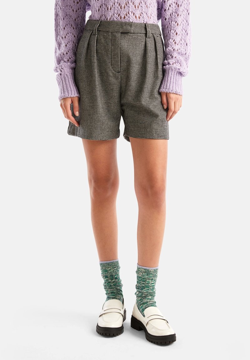 Svartspräckliga shorts med veck, kombinerat med en lavendelfärgad stickad tröja och gröna mönstrade strumpor, bärs med vita loafers.