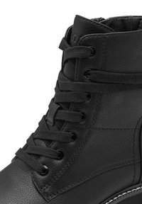 Bottine en cuir noir avec une finition texturée, dotée de lacets ronds, d'œillets en métal et d'une semelle en caoutchouc blanc contrastant.