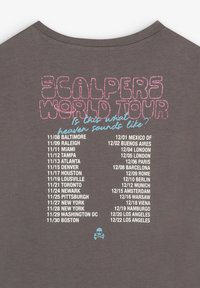 Camiseta gris con un diseño serigrafiado en texto rosa y azul, que detalla "GIRA MUNDIAL SCALPERS" y un icono de calavera en la parte inferior.
