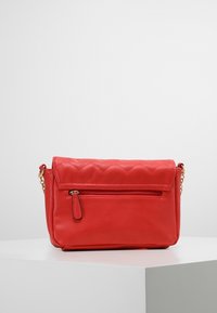 Borsa a tracolla in pelle rossa con patta trapuntata, dotata di una tasca frontale con cerniera e una tracolla a catena dorata. Texture liscia, design compatto.