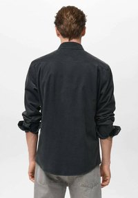 Camisa negra de manga larga con detalles de botones y mangas arremangadas, confeccionada en una tela suave, con un cuello estándar y costura en la yugo trasero.