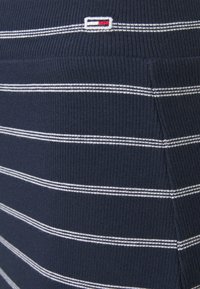 Námornícky modrý pruhovaný textil s bielými a šedými horizontálnymi pruhy, s malým vyšitým logom v levom hornom rohu.