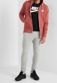 Red zip-up hoodie, black graphic T-shirt, grey slim-fit sweatpants, and black sneakers. Features Nike logo on hoodie and T-shirt.