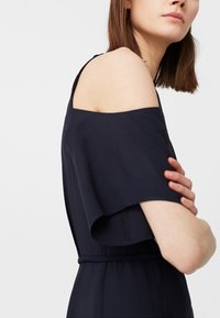 Granatowa sukienka z odkrytymi ramionami i krótkimi, zwiewnymi rękawami. Posiada dopasowaną talię oraz gładką fakturę. Prosty, elegancki fason.