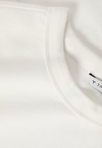 Κοντινή λήψη λευκού βαμβακερού T-shirt με στρογγυλή λαιμόκοψη που δείχνει τη ραφή στη λαιμόκοψη και μέρος μιας ετικέτας ρούχου.