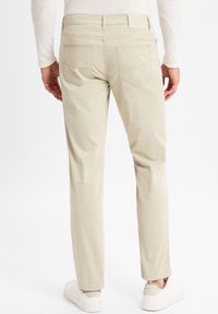 Beige broeken met een rechte pijp, gemaakt van gladde katoenen stof. Twee achterzakken met een subtiele textuur. Draagt met witte sneakers.