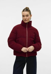 Burgundy corduroy pufferjakke med høj krave og frontlynlås, der har et quiltet mønster og ribbede manchetter.