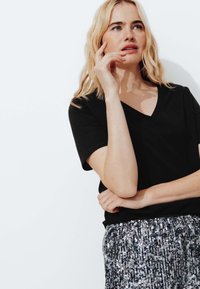 Haut noir à col en V et manches courtes associé à une jupe argentée pailletée. Le haut a une texture douce, tandis que la jupe présente une surface brillante et réfléchissante.