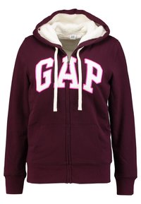 Sweat à capuche zippé couleur bordeaux avec doublure en polaire blanche, cordons de serrage blancs, et grand texte blanc "GAP" bordé de rose sur la poitrine.