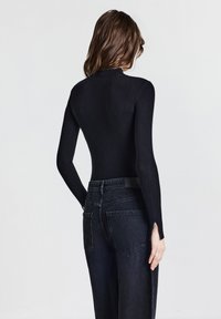 Schwarzes, geripptes Rollkragenoberteil kombiniert mit hoch taillierten, lässig geschnittenen schwarzen Jeans aus Denim mit seitlichen Schlitzen an den Säumen.