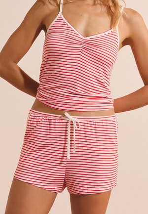Donna che indossa un top senza maniche a righe orizzontali rosse e bianche e pantaloncini abbinati con coulisse in vita.