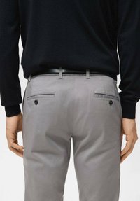 Pantaloni grigio chiaro in tessuto liscio con vestibilità slim, dotati di vita con cintura, tasche posteriori con dettagli a bottone e cuciture impunturate.