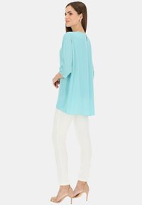 Jasnoniebieska, zwiewna bluzka z rękawami trzyczwartowymi i rozcięciem z tyłu, w połączeniu z dopasowanymi białymi spodniami i cielistymi szpilkami. Gładka tekstura.