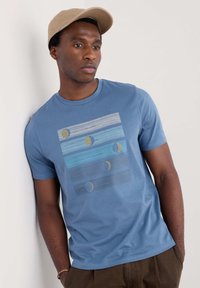 Blå bomullströja med horisontella ränder i varierande nyanser av blått med gula och gråa cirkelaccenter, rund halsringning och korta ärmar.