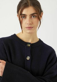 Marinblå cardigan i mjukt material, med rund halsringning och tre stora knappar, ribbade ärmslut och en avslappnad passform.