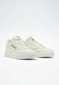 Białe skórzane sneakersy o niskim kroju, z perforowanym noskiem, okrągłymi sznurowadłami i metalowym logo Reebok jako akcentem z boku.