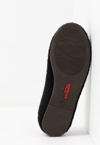 Pantofole in lana nera con una suola in gomma marrone texturizzata che presenta un logo rosso. La suola è dotata di una superficie con motivo per garantire aderenza.