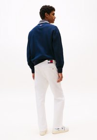 Sweat-shirt navy avec col rayé, jeans blancs et baskets blanches. Marquage notable sur le col et les jeans. Coupe slim et design décontracté.