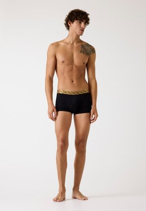 Boxer slip neri con una cintura elastica a motivo dorato, realizzati in un tessuto liscio, con un design aderente e gambe di lunghezza media.