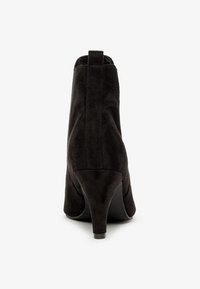 Schwarze Wildleder-Stiefelette mit schmalem Absatz, die eine glatte Oberfläche und ein minimalistisches Design aufweist. Die Rückansicht hebt das elastische Seitenpaneel hervor.