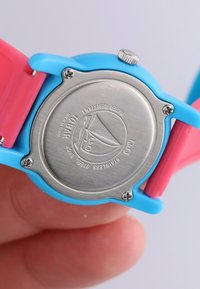 Kleurrijk horloge met een blauwe siliconen band en roze accenten. RVS achterkant met waterbestendigheid en logo details.