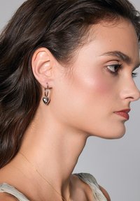 Srebrne kolczyki w kształcie kół z sercem ozdobionym kwiatowym wzorem, noszone na uchu modelki, ukazujące ich wypolerowaną teksturę.