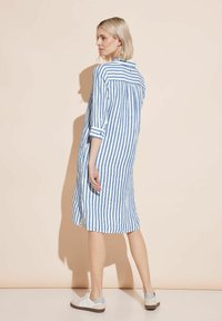 Randig skjortklänning i blått och vitt, tillverkad av lättviktig fabric, har långa ärmar, en knappstängd krage och sidofickor för enkel rörelse.