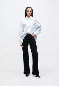 Luźna koszula z dużymi, pionowymi, jasno niebiesko-białymi paskami, zapinana na guziki, z kołnierzykiem, w zestawieniu z czarnymi, rozszerzanymi spodniami oraz czarnymi szpilkami z ostrym noskiem.