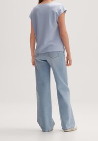 Svetle modrá blůza s krátkým rukávem a volným střihem, kombinovaná s širokými světle modrými džíny. Hladká tkanina s jednoduchým designem.