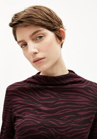 Bordeauxrotes Oberteil mit einem Zebramuster, aus weichem, elastischem Stoff, mit einem hochgeschnittenen Design und langen Ärmeln. Glatte Textur.
