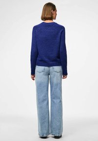 Zils adīts džemperis ar garām piedurknēm, apaļu dekoltē un ribotu apakšmalu; apvienots ar vaļīgiem, gaiši ziliem džinsiem, kuriem ir izbalējusi tekstūra.